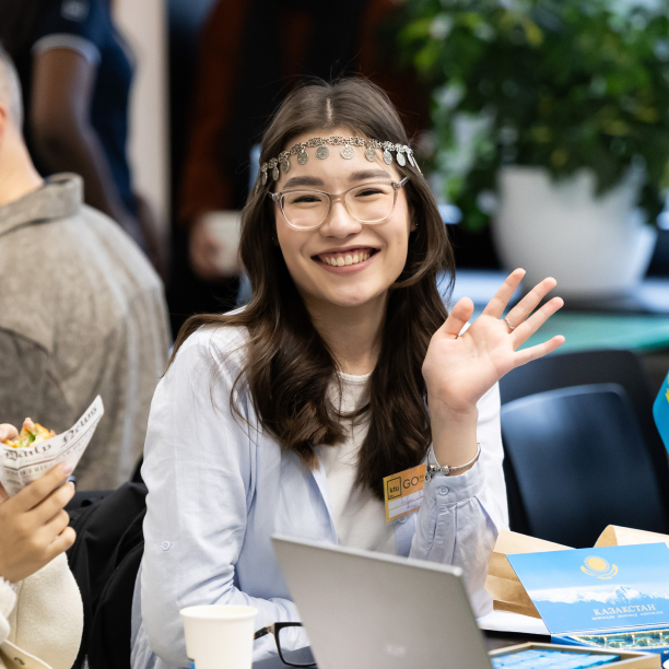 Internationalisation A smiling international student at a KTU event, seated at a table with a laptop and materials representing Kazakhstan, illustrating the University’s international community and global engagement.