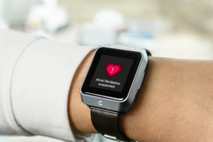A smartwatch on a person’s wrist displays a heart warning icon and the message “Atrial fibrillation suspected.”