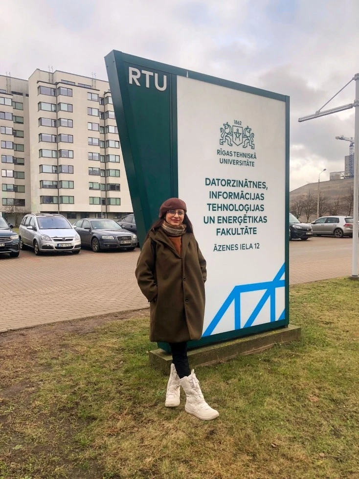 Photo, showing student Umme standing in front of Riga Technical University sign